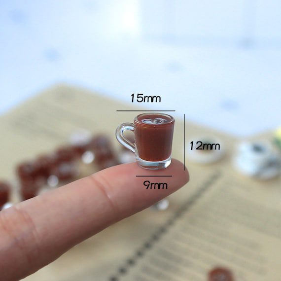 A small cup of coffee on a person's finger.